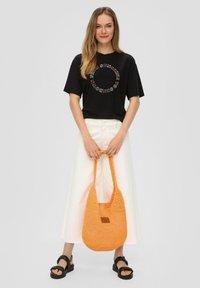 Zwarte T-shirt met cirkelvormige graphic, witte denimroker, oranje gehaakte tas en zwarte platform sandalen; heeft een ontspannen pasvorm en een textuur oppervlak.