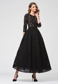 Schwarzes Abendkleid aus Spitze mit Dreiviertelärmeln, einem taillierten Oberteil und einem fließenden A-Linien-Rock, der mit floralen Mustern und einem Gürtel verziert ist.