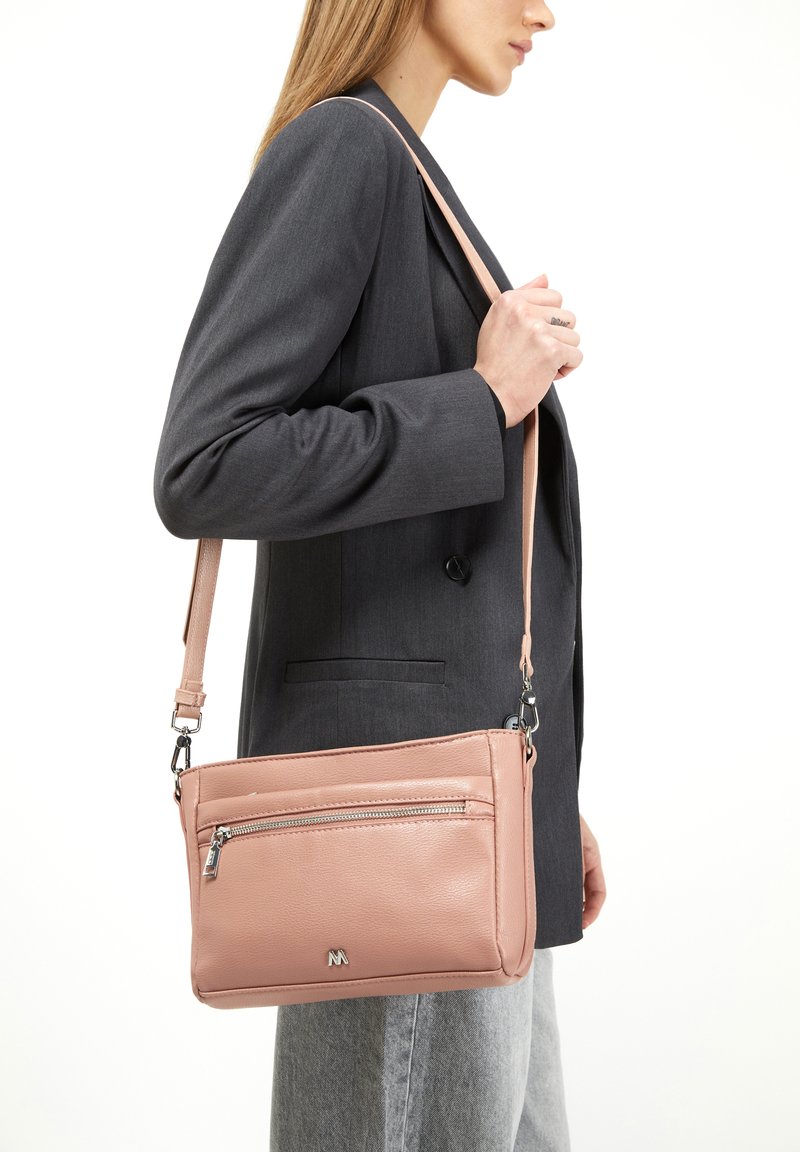 Borsa a tracolla in pelle rosa con tasca anteriore con zip, design slim, tracolla regolabile e dettaglio del logo discreto. Indossata con un blazer grigio.