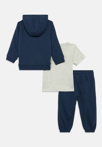 Mørkeblå hættetrøje, grå t-shirt med korte ærmer og mørkeblå joggerbukser med elastisk talje lagt fladt på hvid baggrund.