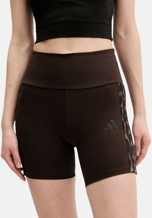 Donna che indossa pantaloncini sportivi neri a vita alta con righe laterali e logo, abbinati a un top nero cropped a coste.