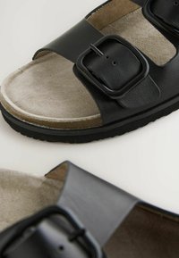 Schwarze Ledersandalen mit einem Schnallenriemen, einer weichen Wildledersohle und einer strukturierten Gummisohle für guten Halt.