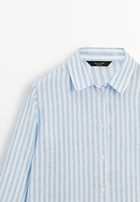 Chemise à rayures verticales bleu clair et blanc avec boutons, col, manches longues et étiquette de marque à l'intérieur du col.