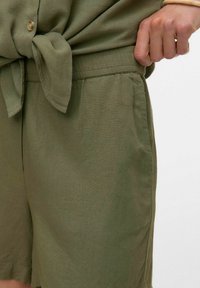 Pantaloni corti in lino verde oliva con vestibilità rilassata, dotati di una cintura annodata e tasche laterali, arricchiti da un tessuto texturizzato.