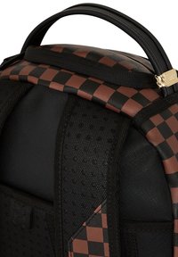 Mochila a cuadros en negro y marrón con una superficie texturizada, correas negras, un asa en la parte superior y acentos de hardware en dorado.