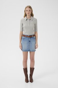 Harmaa lyhythihainen poolopaita, jossa napit edessä, yhdistetty farkkuhameeseen ja ruskeaan nahkavyöhön; päällä ruskeat polven yläpuolelle ulottuvat saappaat.