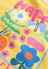 Tissu jaune avec des motifs floraux colorés et ludiques, incluant des fleurs bleues, des accents roses et le mot "HAPPY" en texte en relief.