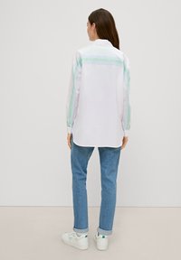 White shirt with light green stripes along the shoulders, paired with light blue jeans and white sneakers. Smooth fabric, relaxed fit.