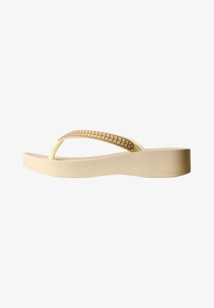 Sandale flip-flop beige à talon compensé avec petits clous ronds décoratifs sur la bride, vue de côté sur fond blanc.