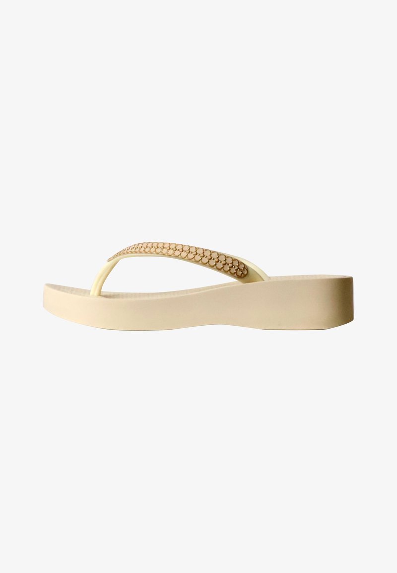 Sandale flip-flop beige à talon compensé avec petits clous ronds décoratifs sur la bride, vue de côté sur fond blanc.