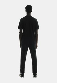 Black cotton t-shirt and matching black pants worn by a person, viewed from the back. The outfit features a simple design, relaxed fit, and solid color.