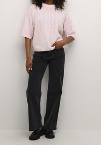 Jasnoróżowy dziergany sweter z teksturowanym wzorem liści, zestawiony z ciemnymi szerokimi jeansami i czarnymi butami.