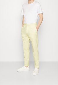 Ljusgula byxor med elastiskt midjeband och sidfickor, matchade med en enkel vit t-shirt och vita sneakers.