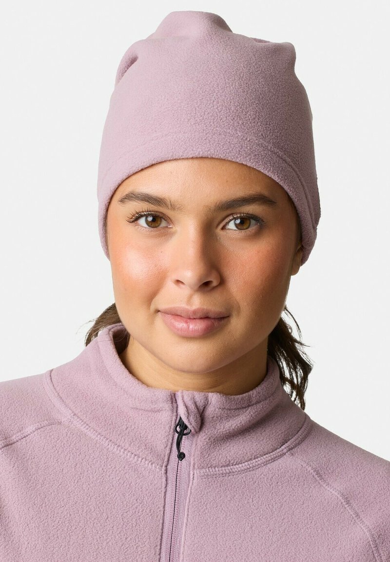 Vaaleanpunainen fleece-pipo, joka istuu tiukasti, joustava pinta ja pyöreä huippu. Yhdistetty yhteen sopivan kaulusvetoketjupuseron kanssa.