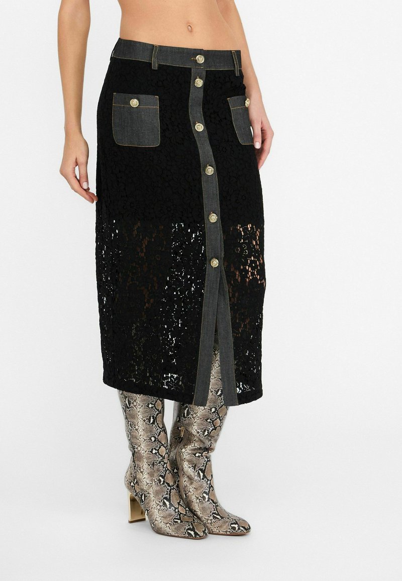 Jupe en dentelle noire avec une taille en denim, ornée de boutons dorés, de deux poches avant et d'un design arrivant au genou. Assortie à des bottes à imprimé serpent brillantes.