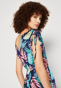 Abito floreale blu navy con foglie vivaci rosa e verdi. Presenta un design off-shoulder, spalle arricciate e vita cinte.