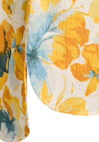 Tissu à motif floral jaune et bleu avec surface texturée et détail d'ourlet incurvé sur fond blanc.