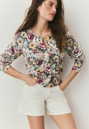 Floralcardigan mit bunten Rosen und Gänseblümchen, Knopfverschluss vorne, gerippte Bündchen, kombiniert mit weißen Shorts, lässiger Schnitt, weicher Stoff.