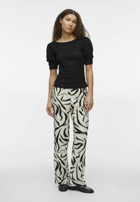 Top din tricot negru texturat cu mâneci bufante și pantaloni largi cu model crem și negru. Modelul stă cu mâinile pe lângă corp pe un fundal simplu.