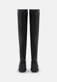 Botas negras hasta la rodilla, hechas de cuero suave, con tacón cuadrado, que presentan un diseño ajustado y costuras verticales sutiles a lo largo del eje.