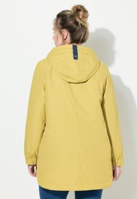 Gul regnjacka med huva, elastiska ärmslut och en blå detalj på baksidan. Har ett slätt, vattentåligt tyg och en skräddarsydd passform.