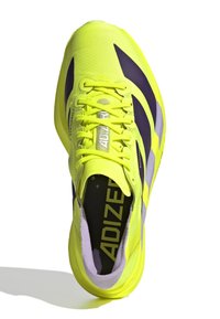 Heldere gele sportschoen met paarse accenten, gestructureerde bovenzijde, brede veters en een clipontwerp. Bevat een logo en een gewatteerde binnenzool.