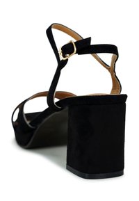 Black suede high-heeled sandal with a chunky block heel. Features an ankle strap with a gold-tone buckle and an open toe design.