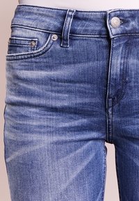 Jeans de mezclilla azul claro con cintura de media altura, diseño de cinco bolsillos y un sutil efecto de desgaste, con acentos de hardware plateado.