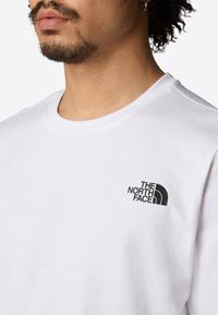 Witte katoenen t-shirt met ronde halslijn en korte mouwen, met een zwart logo op de linkerborst, gladde textuur en casual ontwerp.