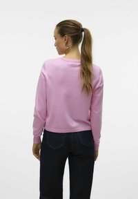 Maglione rosa a maniche lunghe, con texture morbida, scollatura rotonda, polsini a costine, abbinato a jeans blu scuro, visuale posteriore e accessori.