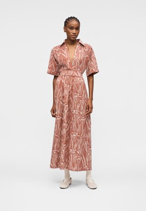 Donna che indossa un vestito midi di colore ruggine con motivo floreale, maniche corte, scollatura a V profonda, cintura in vita e stivaletti bianchi, in posizione rilassata.