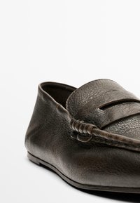 Donkerbruine leren loafers met een gestructureerde afwerking, voorzien van een verhoogde banddetail over de wreef en een lage, flexibele zool.