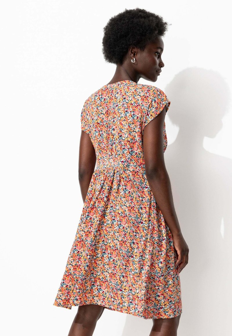 Robe fleurie avec des manches courtes en cap, principalement orange avec des motifs multicolores, en tissu doux, et un design de taille froncée.