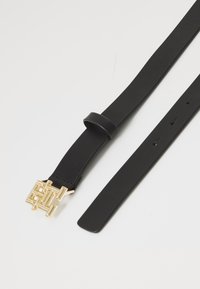 Cintura in pelle nera con una fibbia in metallo dorato geometrica, con una superficie liscia e lunghezza regolabile attraverso più fori.