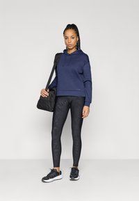 Hoodie azul-marinho, tecido texturizado, com cordão. Leggings pretas com padrão, ajustadas. Ténis pretos de desporto. Bolsa preta com alça de ombro.