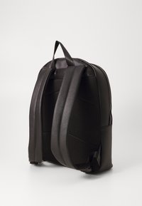 Černý batoh s strukturovanou tkaninou, polstrovanými popruhy a horním držadlem. Má elegantní design a zakřivený tvar pro ergonomické nošení.