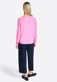 Pull léger rose avec une coupe décontractée, texture côtelée, et un petit logo au dos ; associé à un pantalon large bleu marine et des chaussures noires.