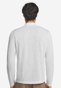 Polo shirt bianco a maniche lunghe realizzato in un tessuto testurizzato, con colletto classico e vestibilità rilassata. Nessun motivo o dettaglio visibile.