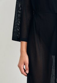 Mustritud musta võrksärki laiade varrukatega. Kude on kerge ja poolläbipaistev, rõhutades naha nähtavust all.