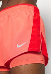 Pantalones cortos deportivos Nike en coral y rojo, con un patrón texturizado, cintura elástica y un pequeño logo blanco en el lado inferior izquierdo.