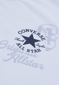 Vaaleansininen puuvillapaita, jossa on tumma tähtigrafiikka, "Converse All Star" -teksti ja hienovarainen harmaa "Original" -kuvio.