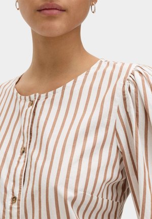 Joven con camisa abotonada de rayas verticales beige y blancas, con escote redondo y pequeños pendientes de aro.