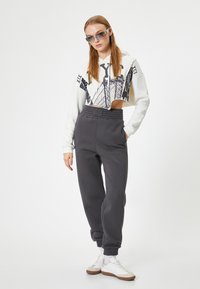Afklippet hvid hoodie med sort grafisk design, parret med mørkegrå sweatpants med elastiske manchetter og talje. Hvide sneakers fuldender looket.