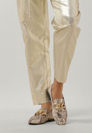 Schlangenleder-Print Slipper mit goldener Kettenakzent, kombiniert mit glänzenden, hellgoldenen Hosen. Die Schuhe haben eine abgerundete Zehenpartie und eine flache Sohle.
