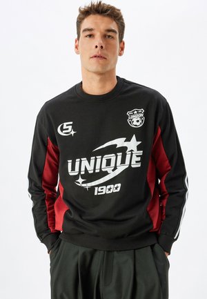 Sudadera negra con paneles laterales en color burdeos, con gráficos en blanco: "UNIQUE 1900" y un logotipo. Cuello y puños acanalados, textura de tela suave.