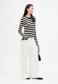 Top de rayas blanco y negro de manga larga combinado con pantalones anchos blancos, accessorios con un pequeño bolso negro y zapatos negros de punta.