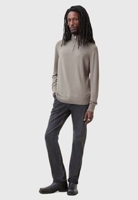 Hellbrauner Reißverschluss-Pullover mit langen Ärmeln, glatte Textur, getragen mit dunkelgrauen Jeans und schwarzen Schuhen. Schlichtes Design, lässige Passform.