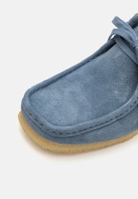 Blauwe suède schoen met een zachte textuur, ronde neus en beige rubberen zool. Beschikt over gestikte details langs de randen en een vetersluiting.