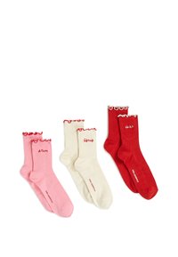 Kolme paria poimullisia sukkia vaaleanpunaisena, kermanvärisenä ja punaisena, joissa on röyhelöreunat ja brodeerattuja ranskankielisiä sanoja valkoisella taustalla.