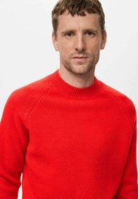 Rde pleten sveter z rebrovanim okroglim izrezom, raglan rokavi in mehak tekstur. Ni vidnih vzorcev ali dodatkov.